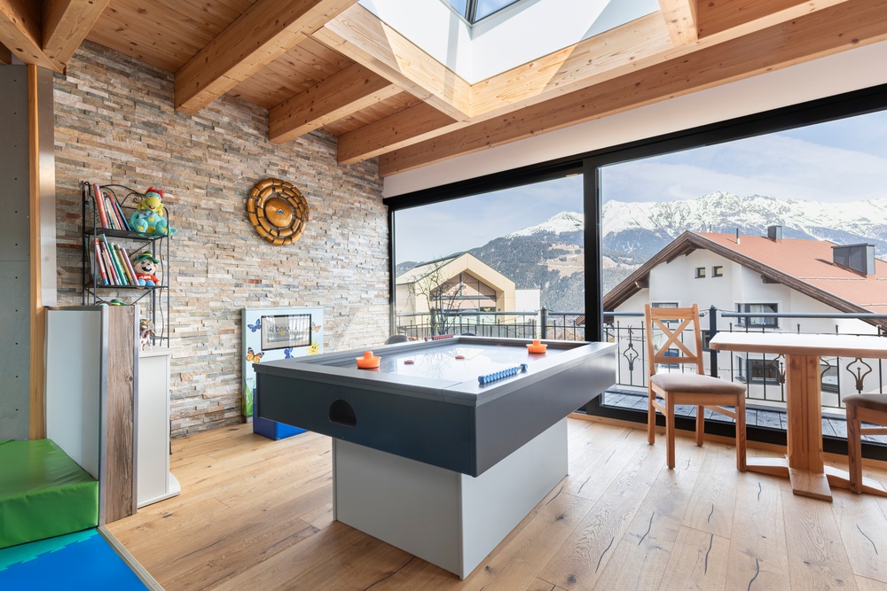 Ein helles Spielzimmer in Mimis Kinderspielwelt im Alpenapart in Ladis mit Airhockey und Bergblick.