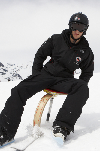 Inmitten einer verschneiten Berglandschaft sitzt eine Person in schwarzer Skiausrüstung und Helm selbstbewusst auf einem Snowbike. In den Brillen spiegeln sich der helle, bedeckte Himmel und die fernen Gipfel. Sie verkörpert den abenteuerlichen Geist eines Aktivurlaubs in Serfaus-Fiss-Ladis – perfekt für Sommer- oder Winterausflüge.