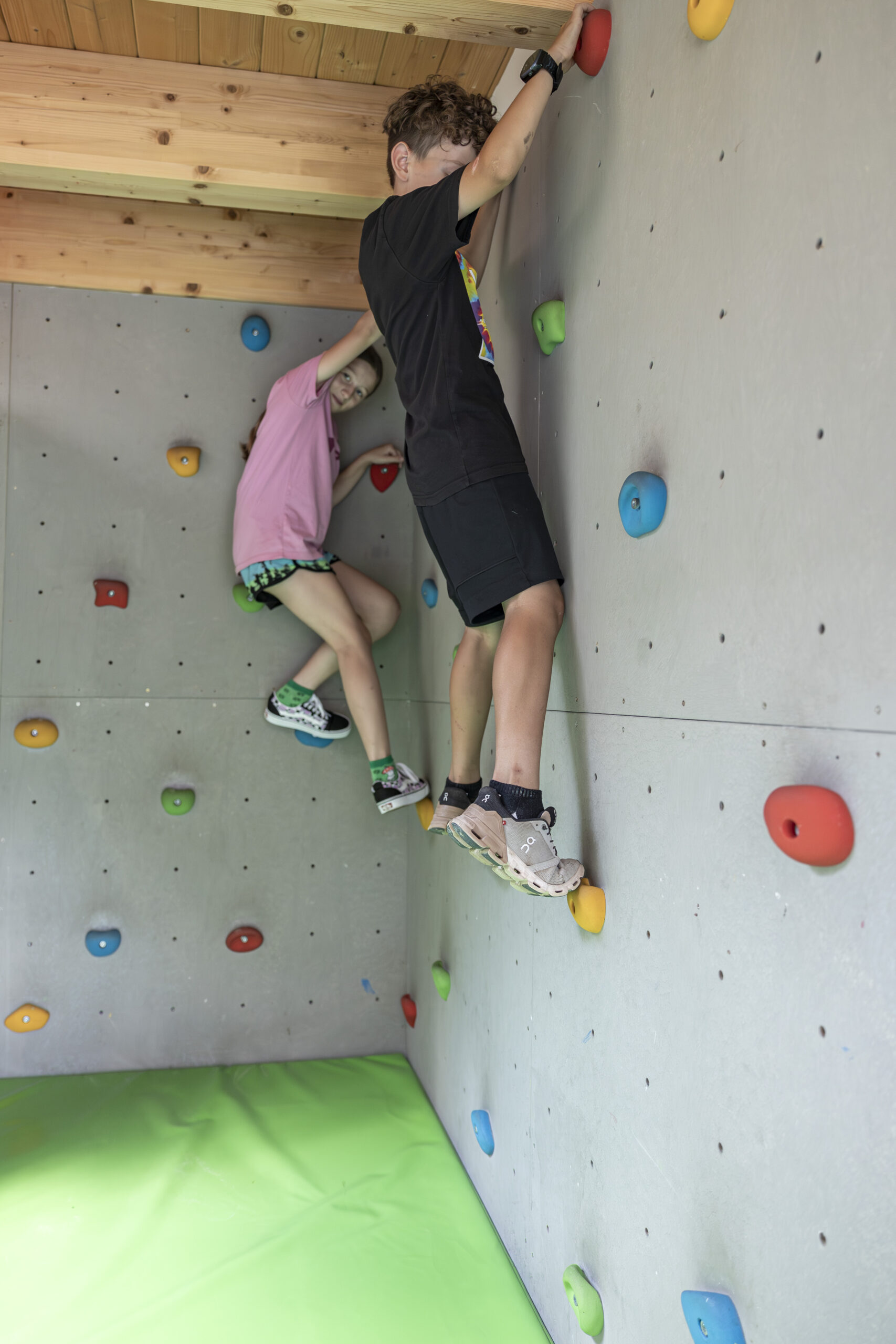 Zwei Kinder klettern in Mimis Kinderspielwelt im Alpenapart in Ladis an einer bunten Boulderwand.