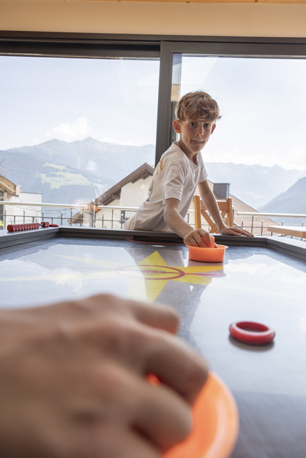 Junge spielt Airhockey in der Mimis Kinderspielwelt im Alpenapart in Ladis, im Hintergrund die Berge.