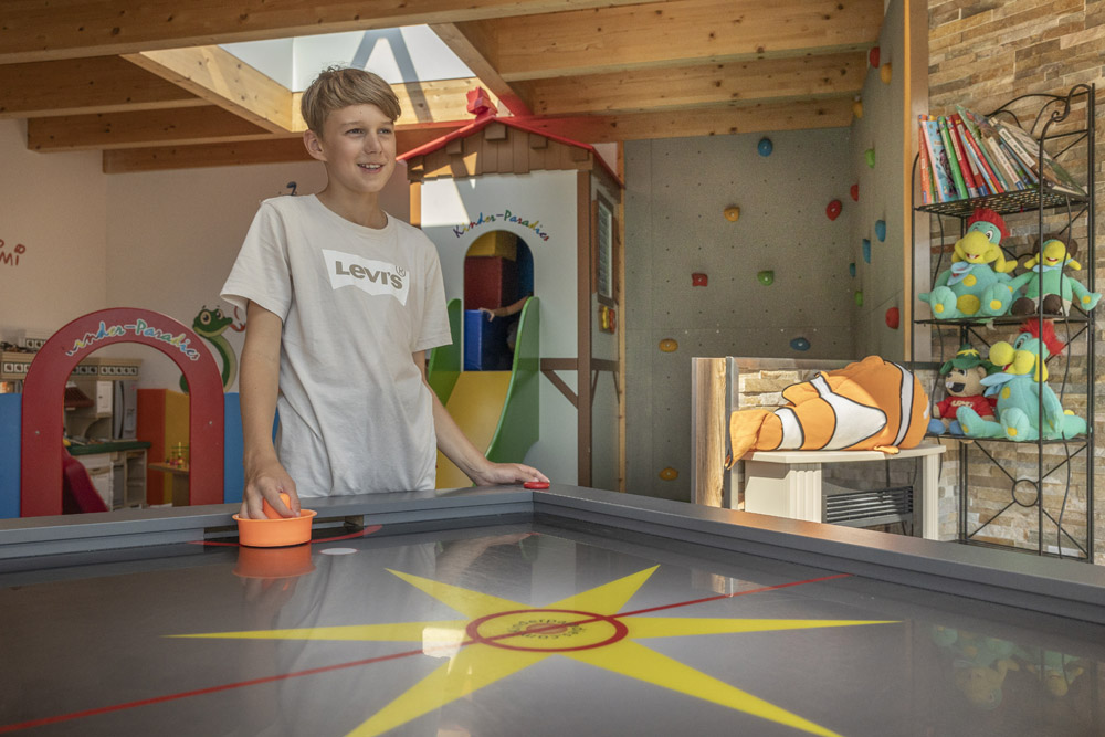 Ein Junge spielt Airhockey in Mimis Kinderspielwelt im Alpenapart in Ladis, umgeben von Spielzeug.