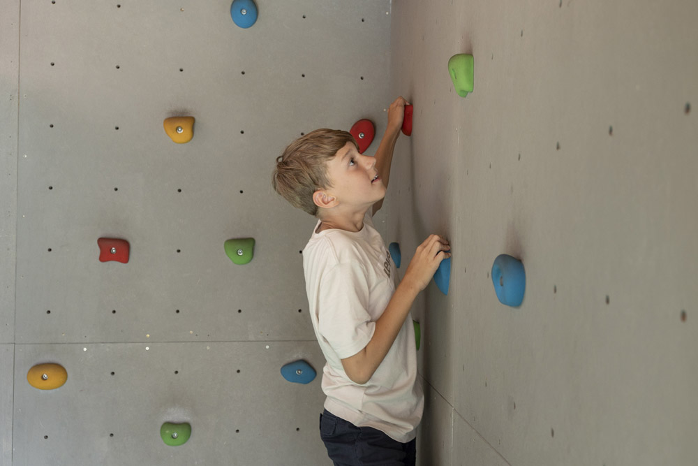 Junge beim Klettern an der Indoor-Felswand in Mimis Kinderspielwelt im Alpenapart in Ladis, Blick nach oben.