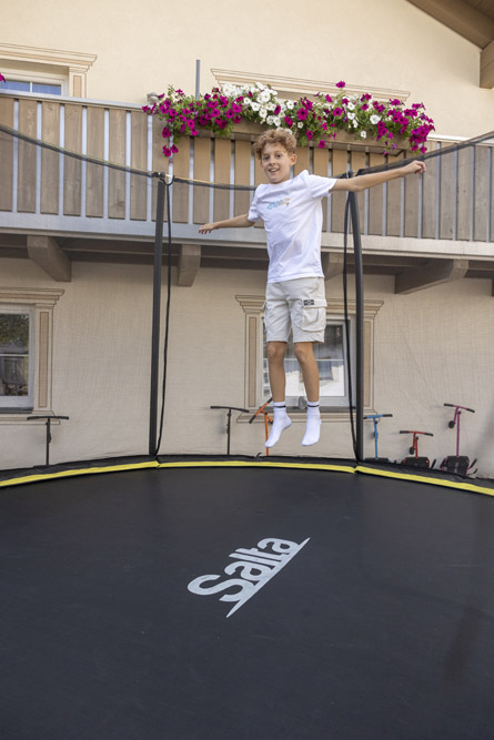 Lächelnder Junge im weißen Hemd springt auf einem Trampolin in Mimis Kinderspielwelt im Alpenapart in Ladis.
