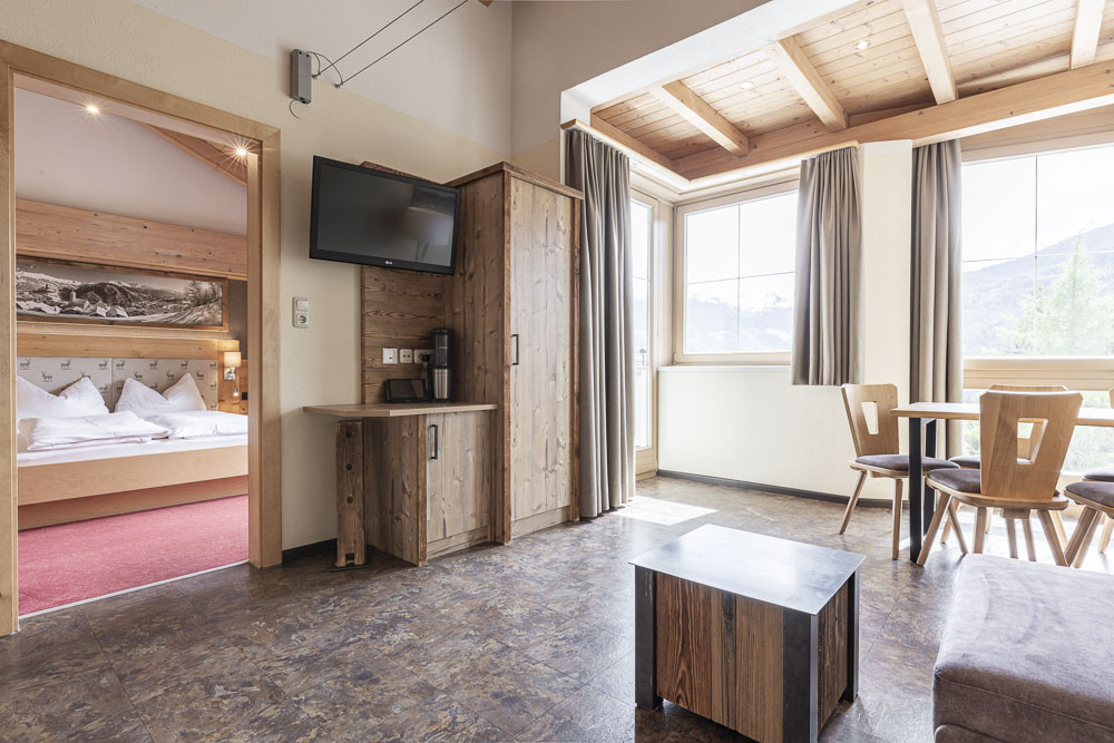 Ein gemütliches Apartment in Ladis, ideal für 4-5 Personen, ist mit rustikalen Holzmöbeln eingerichtet. Es verfügt über ein Bett in einem angrenzenden Raum, einen an der Wand montierten Fernseher, einen kleinen Tisch mit Stühlen und große Fenster mit Blick auf die Berge. Die Decke zeigt sichtbare Holzbalken.