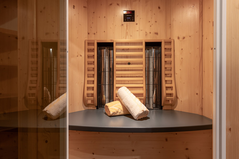 Das Apartment Morgensonne für 2-4 Personen in Ladis bietet einen ruhigen Rückzugsort mit einer Infrarotsauna aus Holz. Im Inneren finden Sie zwei aufgerollte Handtücher auf einer grauen Bank, hellbraune holzgetäfelte Wände und Heizelemente hinter einem Schutzgitter, die alle über das kleine Bedienfeld an der Decke gesteuert werden.
