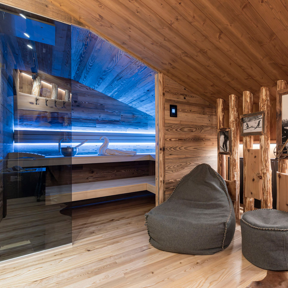 Experience the cozy wooden sauna room at the Laudegghof, featuring a modern glass sauna illuminated in blue. This inviting sanctuary includes comfortable gray bean bag chairs and wood paneling, perfectly complementing the serene garden spa with a whirlpool for ultimate relaxation.