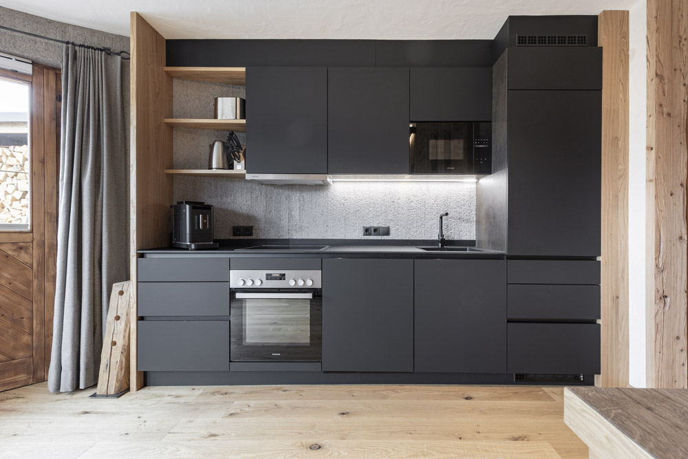 Moderne Küche mit schwarzen Schränken, Backofen, offenen Regalen und Holzakzenten.