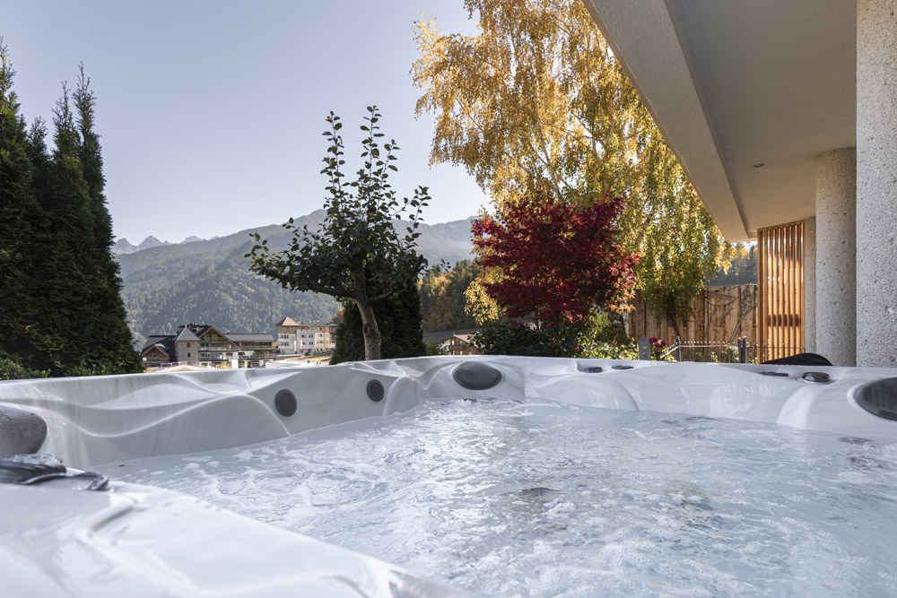 Whirlpool im Freien mit sprudelndem Wasser, Blick auf Bäume und ferne Berge an einem sonnigen Tag.