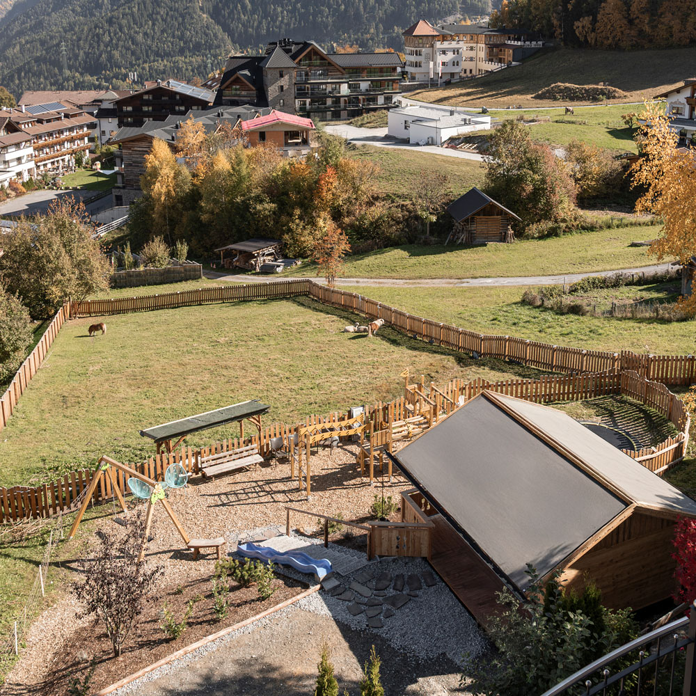 A fenced playground and grassy field at Mimis Kinderspielwelt for Kids at the Alpenapart in Ladis.