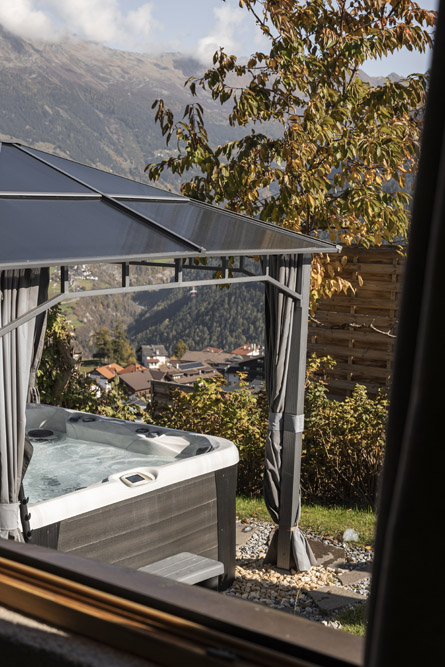 Whirlpool im Freien unter einem Vordach mit Blick auf die Berge und das Dorf im Hintergrund.
