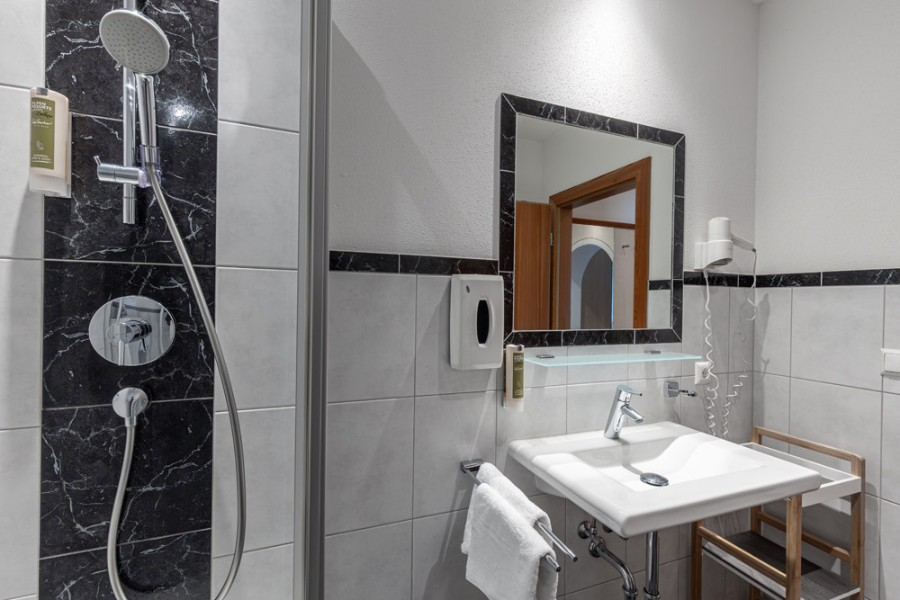 Modernes Badezimmer mit Dusche, Waschbecken, Spiegel, Handtuchhalter und Wandhaartrockner.