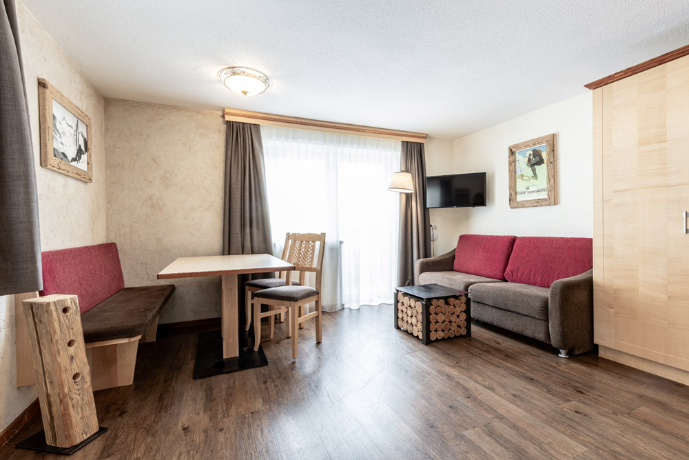 Heller Wohnbereich mit Sofa, Tisch, Stühlen, Wandkunst und großem Fenster mit Vorhängen.