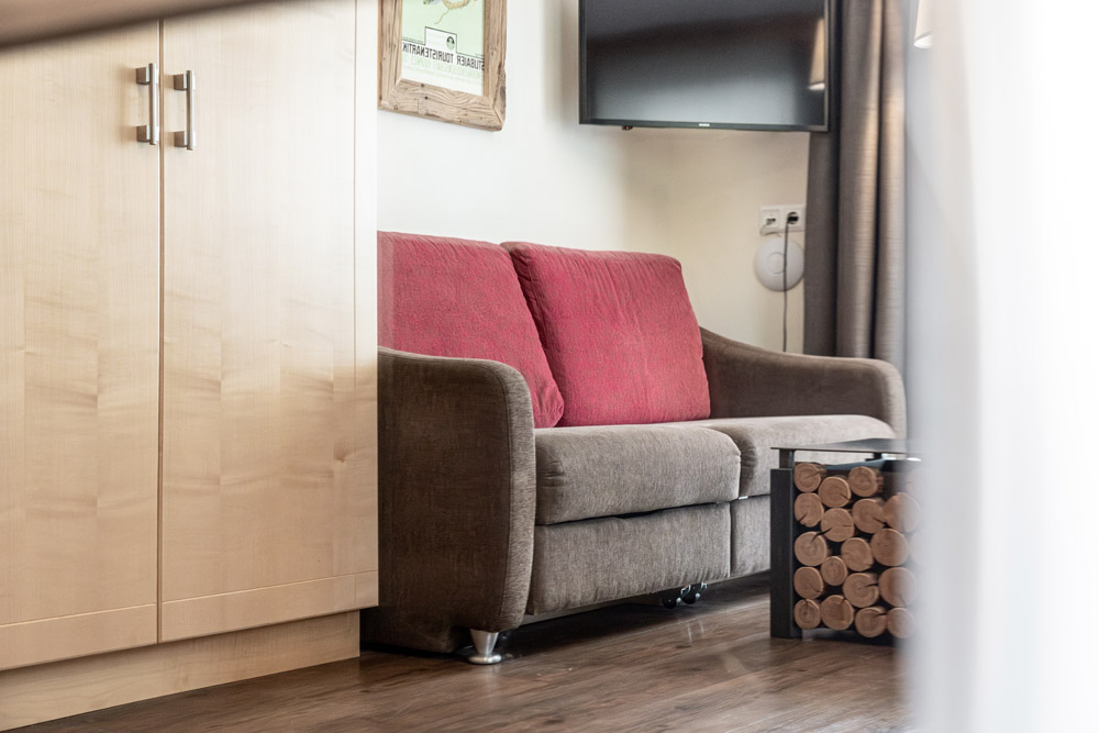 Braunes Sofa mit roten Polstern neben einem Schrank und einem Beistelltisch aus Holz in einem Wohnzimmer.