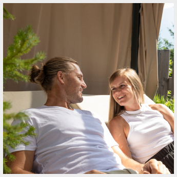 Ein Mann und eine Frau in den Alpenresorts lächeln sich an, während sie sich an einem sonnigen Tag im Freien entspannen.