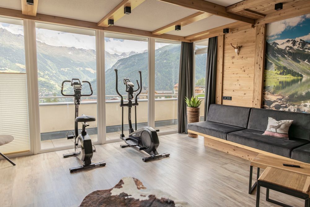 Moderner Raum mit zwei Heimtrainern, großen Fenstern, einem Sofa und Blick auf die Berge.