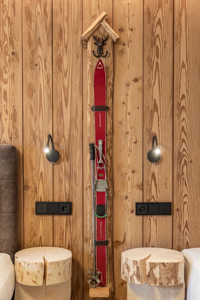 Ein roter Vintage-Ski, befestigt an einer Holzwand zwischen zwei Holzhockern und zwei Wandleuchten.