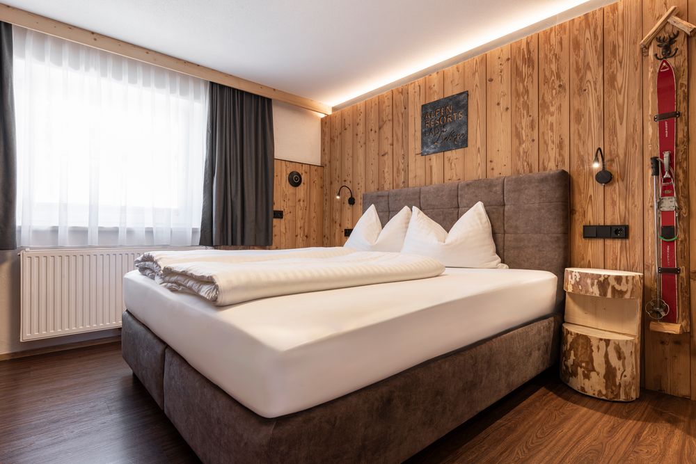Gemütliches Schlafzimmer mit Holzwänden, einem großen Bett, rustikaler Einrichtung und Vintage-Skiern an der Wand.