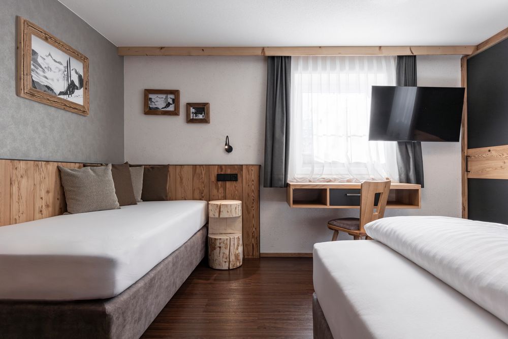 Minimalistisch eingerichtetes Hotelzimmer mit zwei Betten, einem an der Wand montierten Fernseher, einem Schreibtisch, einem Fenster und Holzakzenten.