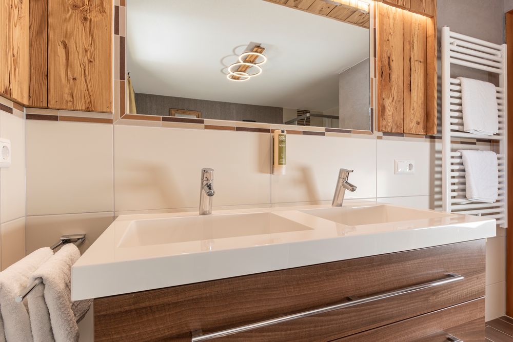 Modernes Badezimmer mit Doppelwaschbecken, Holzschränken, Spiegel und Handtuchhalter mit gefalteten Handtüchern.