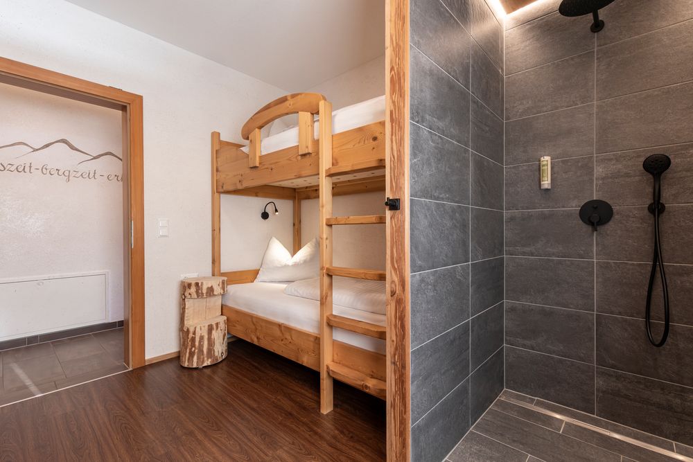 Holz-Etagenbetten und eine moderne, mit grauen Fliesen ausgekleidete Dusche in einem gemütlichen, rustikalen Zimmer.