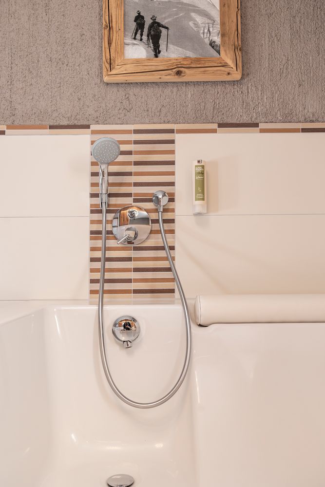 Moderne Badewanne mit Duschkopf, gestreiften Akzentfliesen und einem gerahmten Foto über der Wanne.