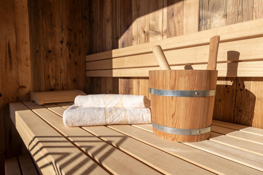 Innenraum einer Holzsauna mit zwei gefalteten Handtüchern und einem Holzeimer auf einer Bank.