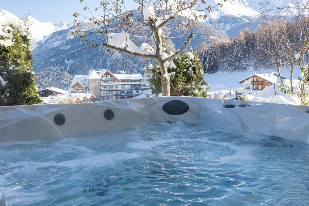 Whirlpool im Freien mit Strömung, verschneiten Bäumen und Bergen im Hintergrund.
