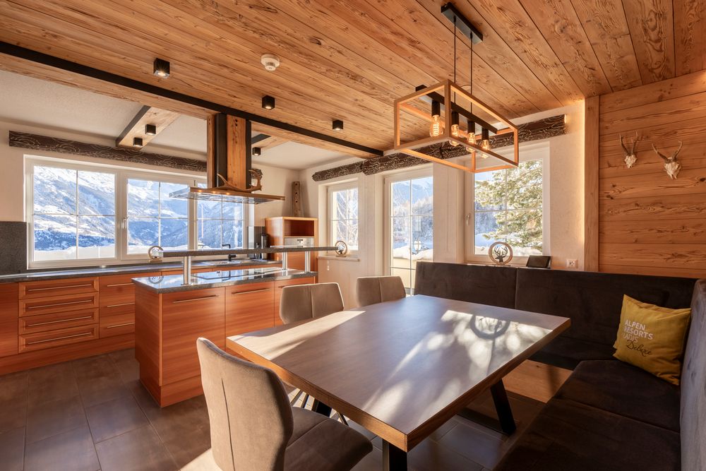 Moderne Küche und Essbereich aus Holz mit großen Fenstern, die den Blick auf verschneite Berge freigeben.
