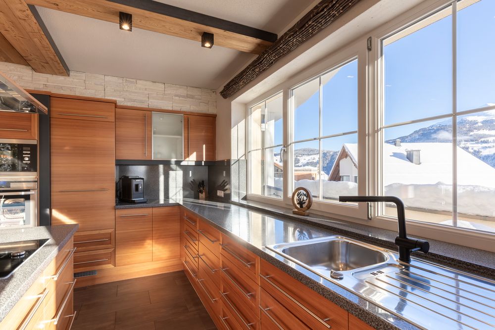Moderne Holzküche mit großen Fenstern, die den Blick auf verschneite Berge und Dächer freigeben.
